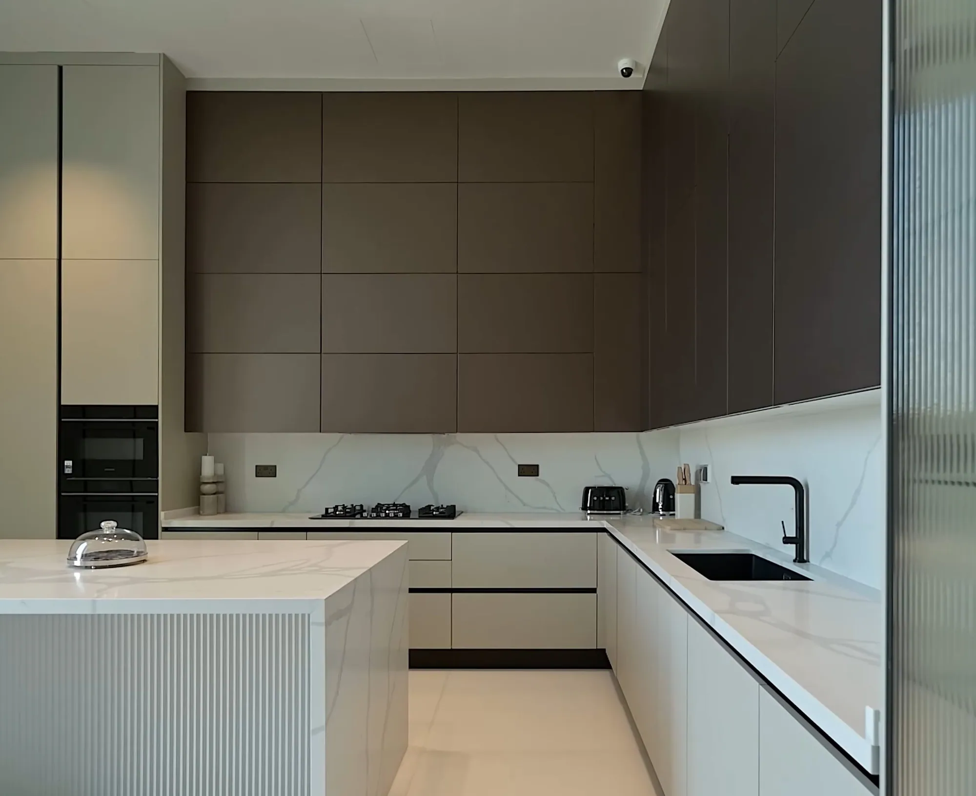 Taupe and white L-shaped kitchen with marble splashback and reeded island